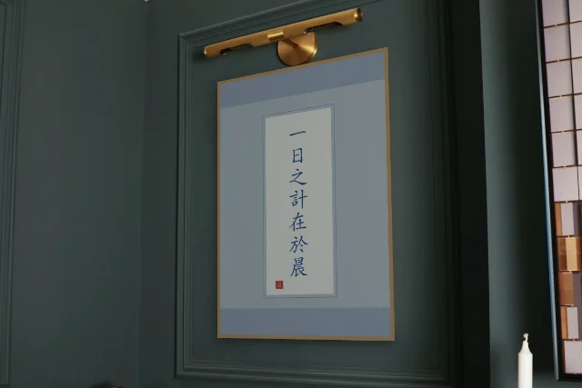 La journée se décide au matin en rouleau, porcelaine bleue : affiche encadrée chêne sous une lampe de tableau, mur vert profond